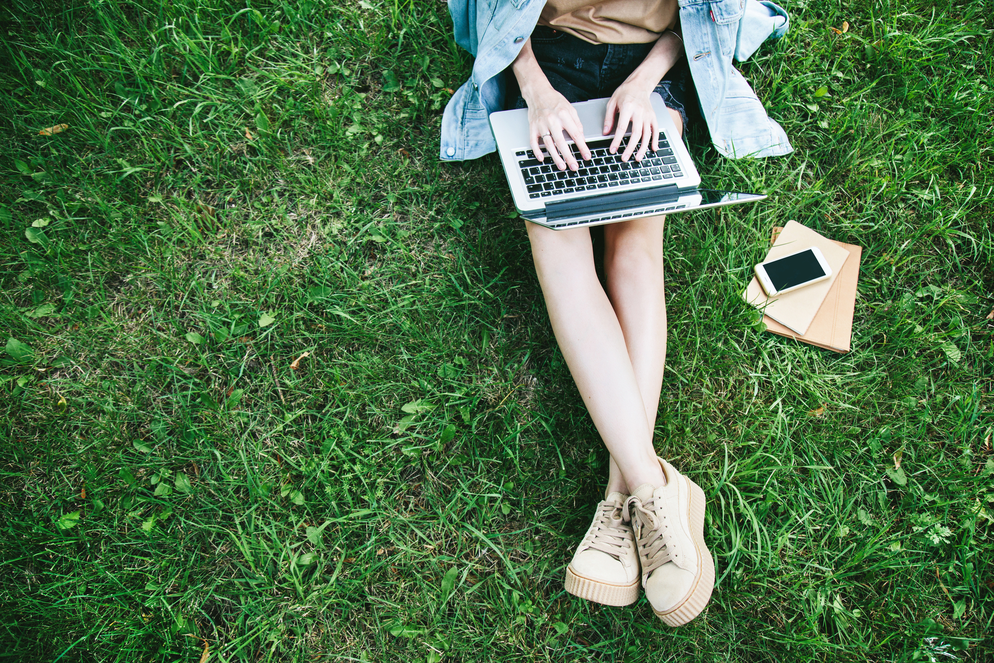 A person sitting on the grass working on laptop